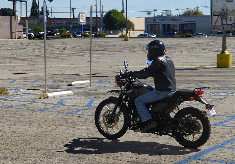 rider on a small Himalayan motorcycle in an empty parking lot
