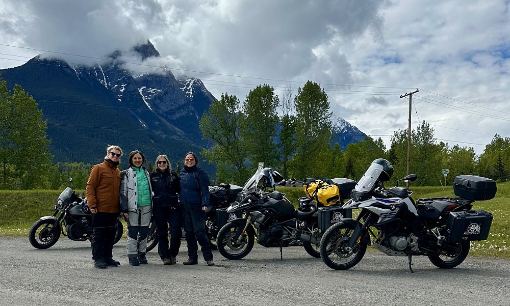 four women and their motorcycles with a cloud-shrouded mountain looming in the background