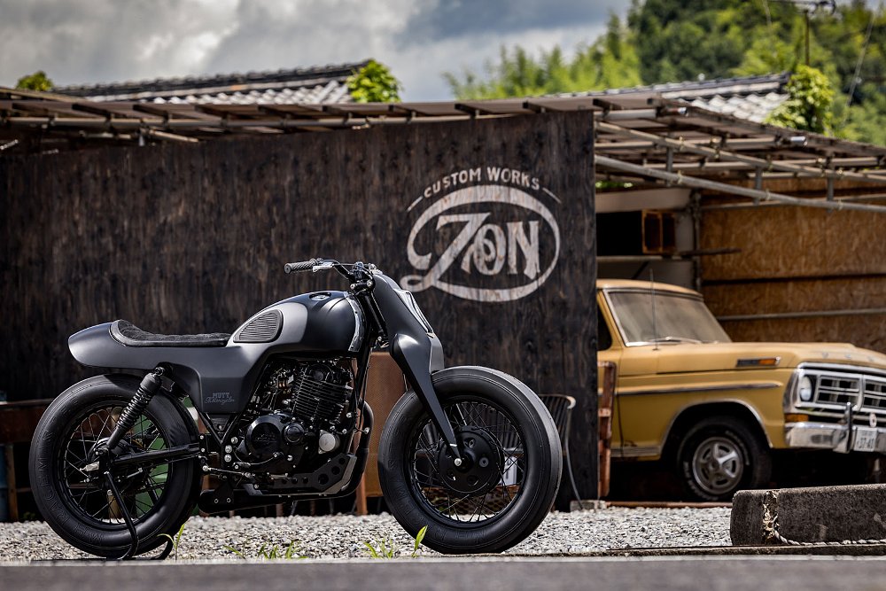 side view of the retro, black custom Mutt with an old truck in the background