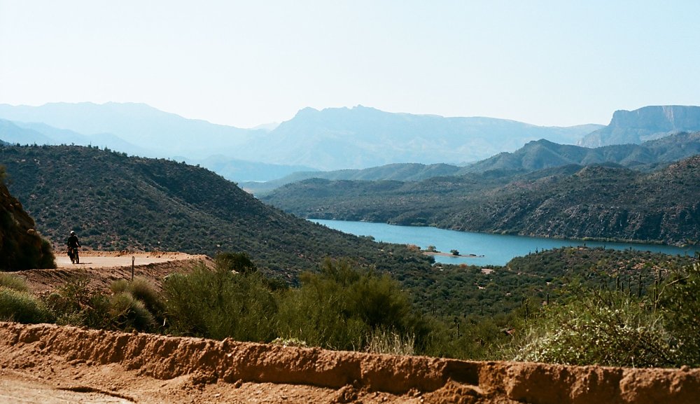 distant view of a rider on a dirt road by a lake
