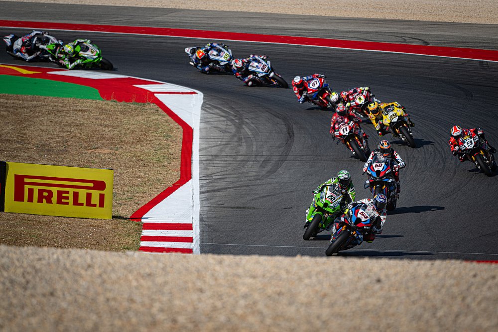 a tight field of motorcycles races through a curve at the start of the race in Portimao