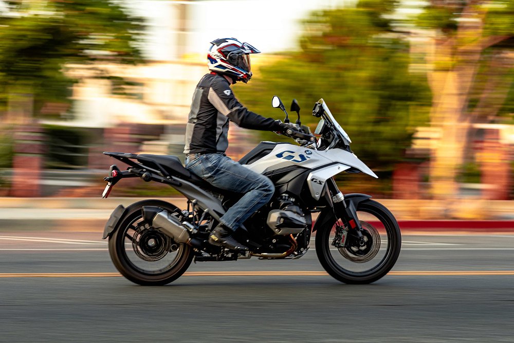 2024 BMW R 1300 GS riding down a city street with trees blurred in the background.
