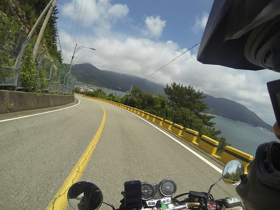 rider's view aboard the motorcycle on a road along the ocean with mountains on the left