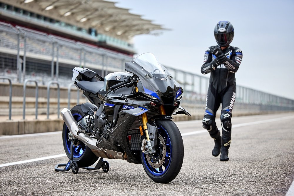 rider in leathers approaching an R1M parked on a race track