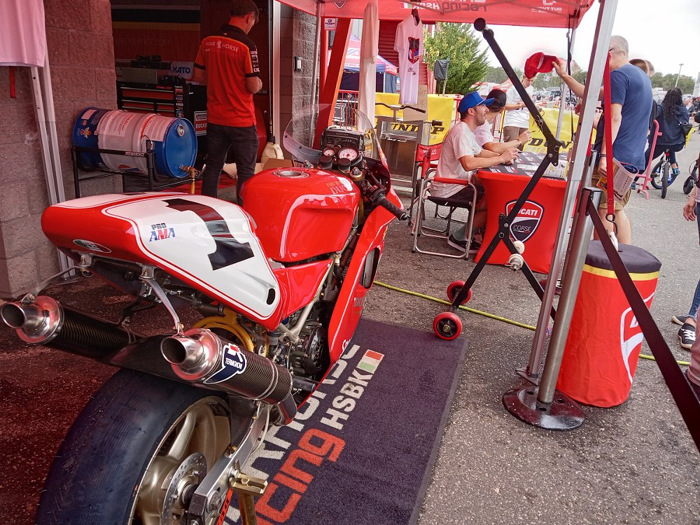 Troy Corser race bike in foreground, Herrin signing an autograph for a fan in the background