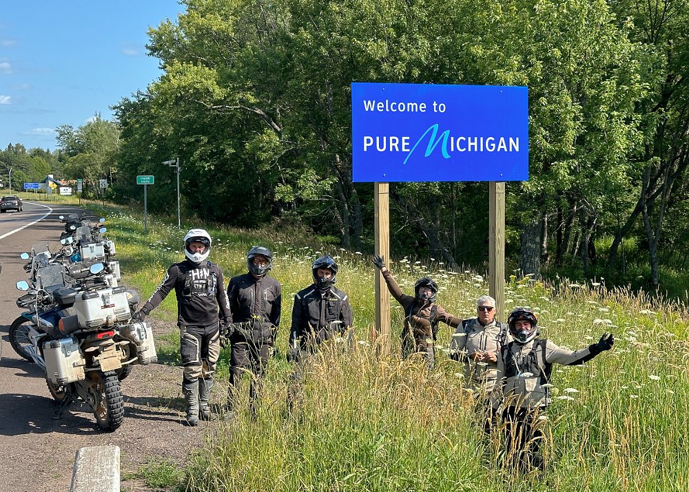 riders standing under a welcome to Michigan sign