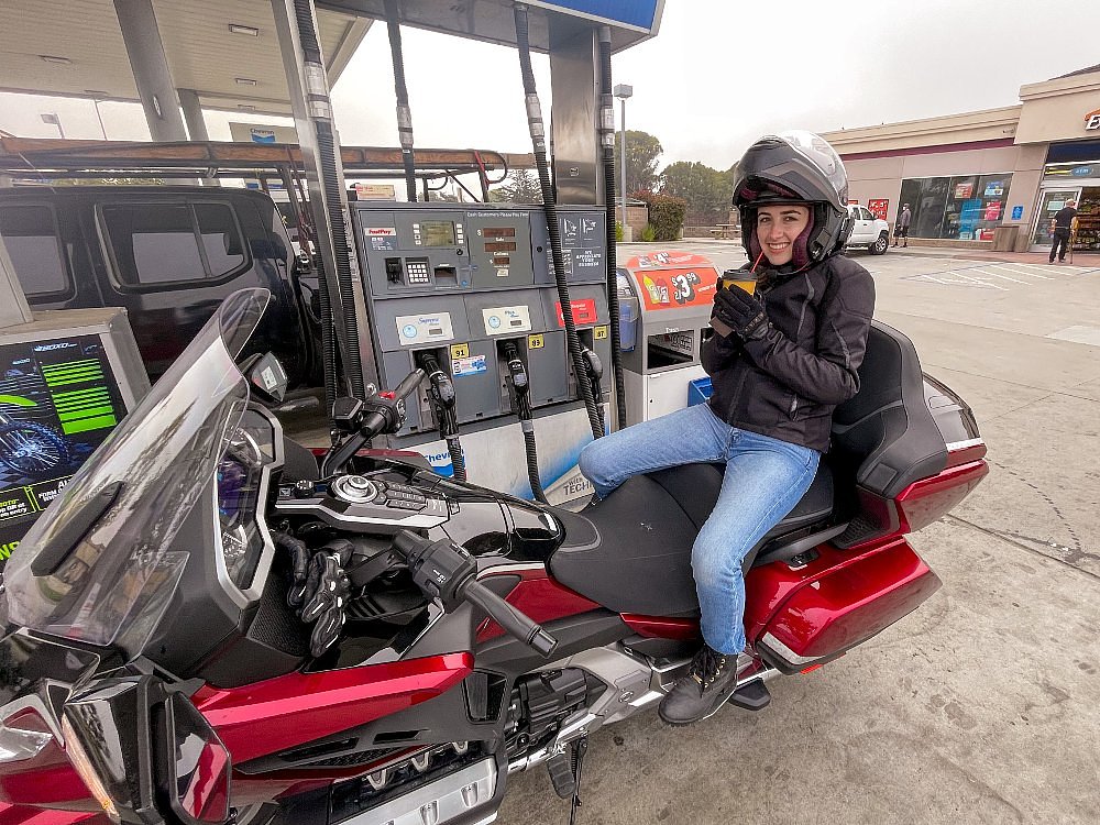 woman sitting on the rear seat of the Gold Wing drinking a coffee beside the gas station pumps at a stop