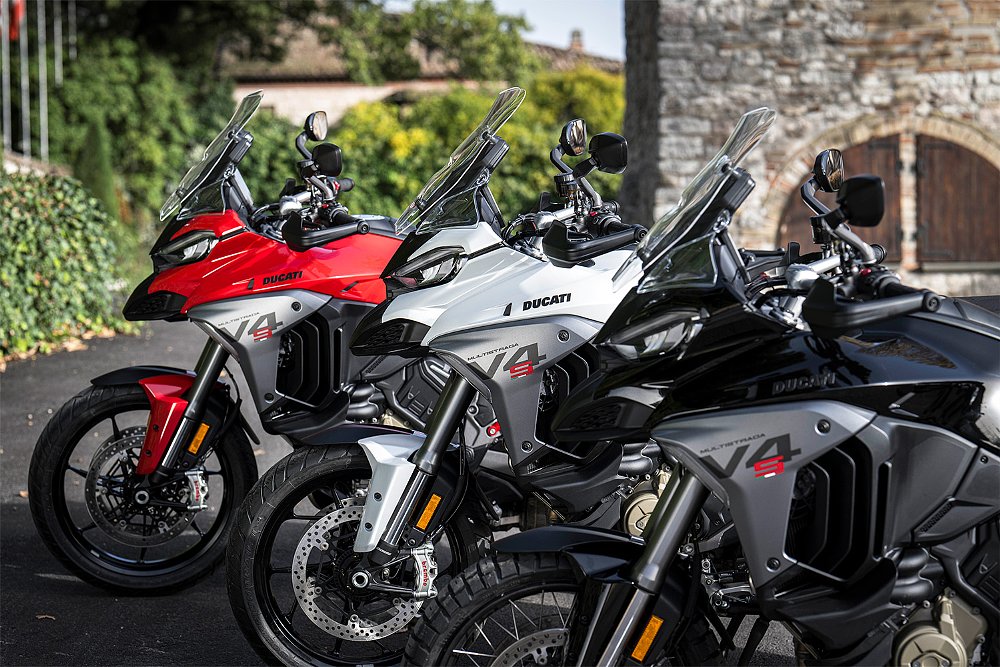 Three 2025 Multistrada V4 S motorcycles of various colors parked outside the Park Hotel ai Cappuccini in Gubbio, Italy.