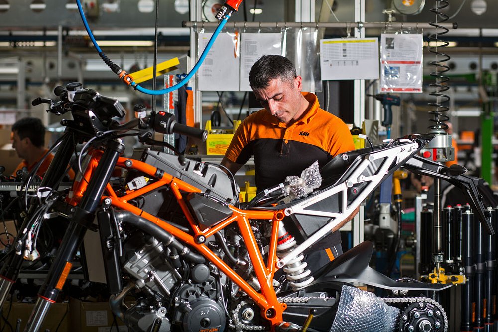 man working on the frame of a partially assembled KTM motorcycle in the factory