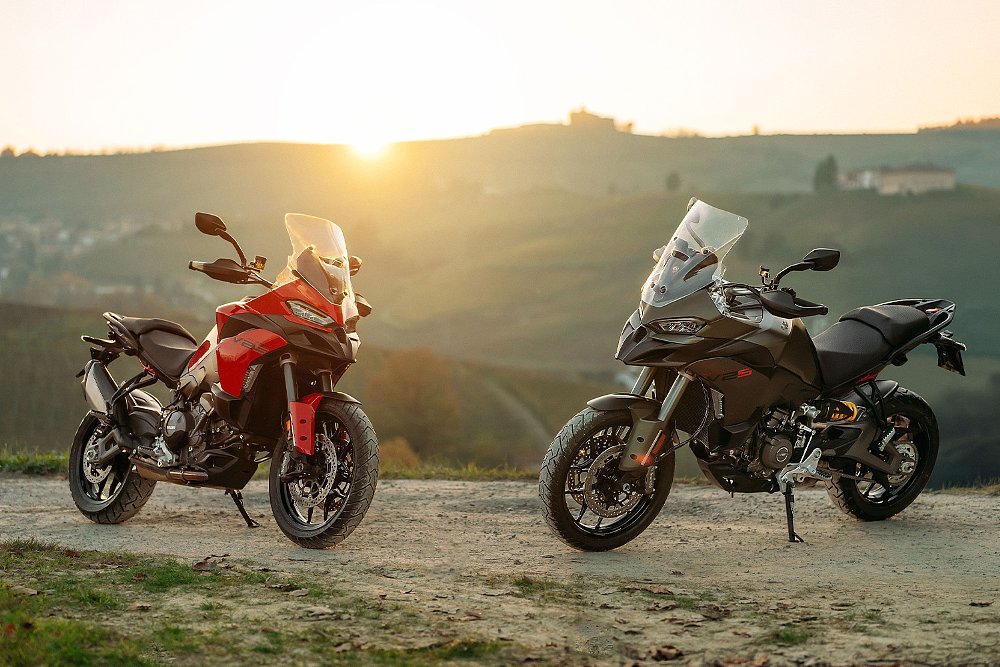 Two 2025 Ducati Multistrada V2 S models parked on atop a hill with the sun setting in the background.