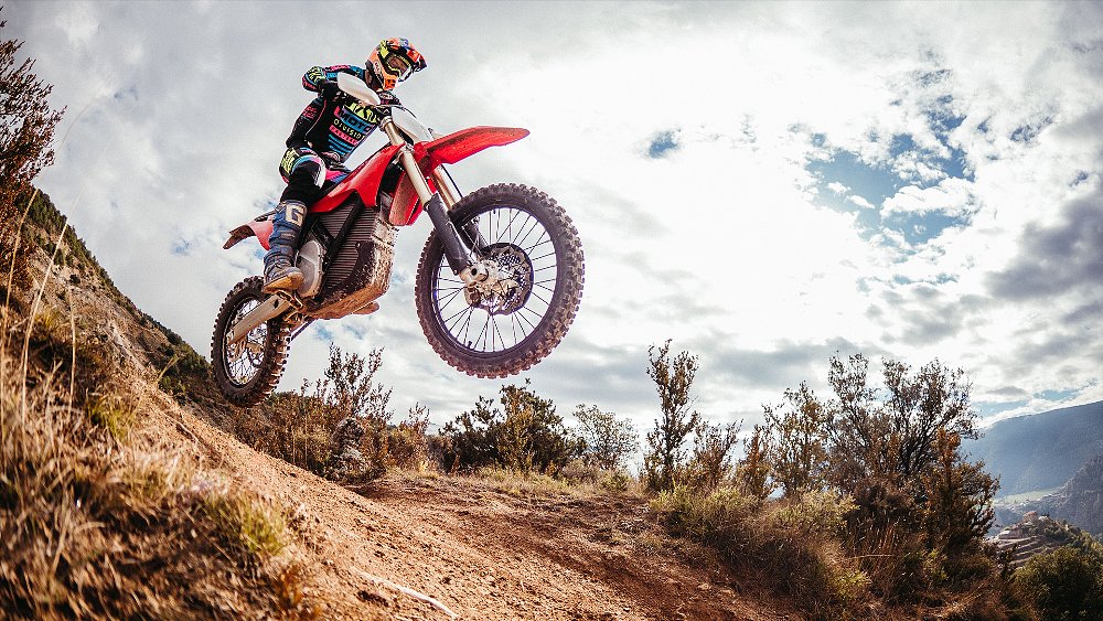 A dual-sport rider wheelies the Stark VARG EX over a hill. 