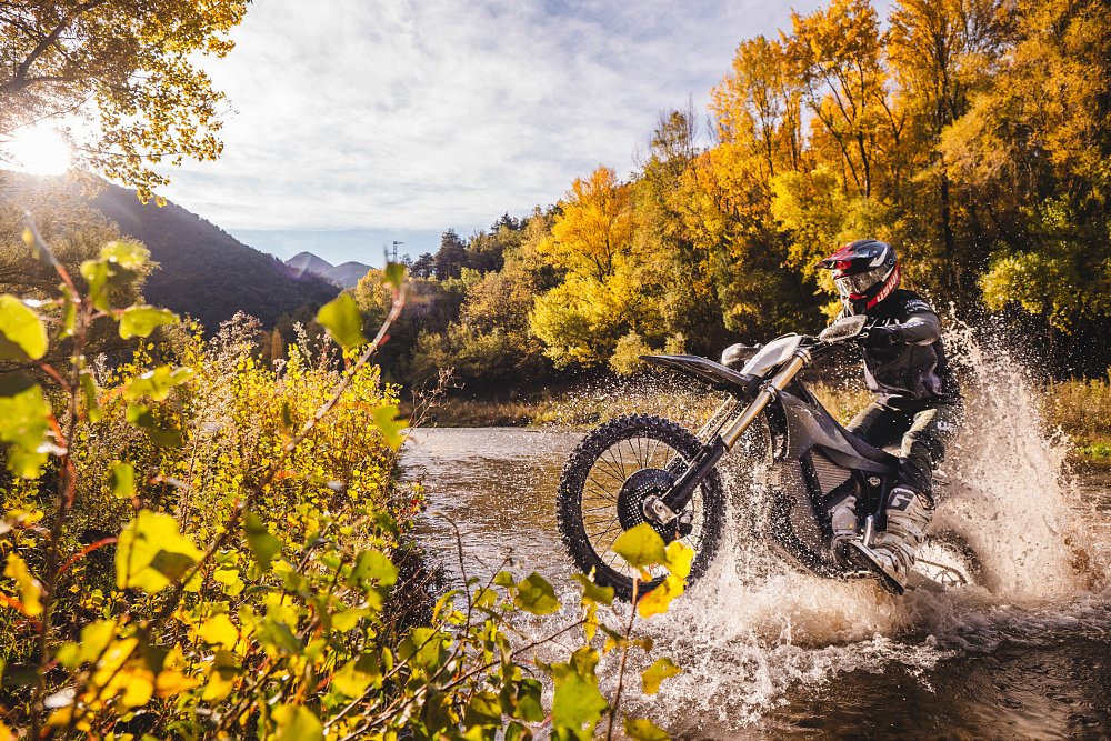 An enduro rider crosses a river aboard a Stark VARG EX. 