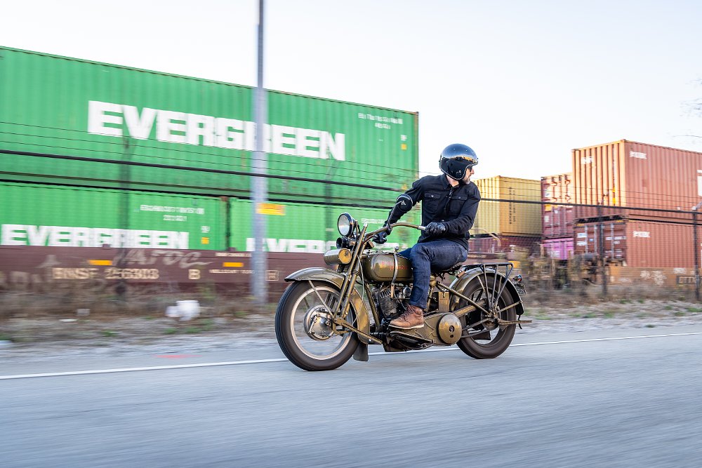 1924 Harley-Davidson Model J riding next to a freight train, with the rider looking behind.