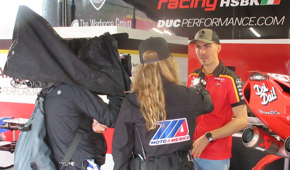 racer Loris Baz being interviewed on camera in the Ducati paddock area at a MotoAmerica race