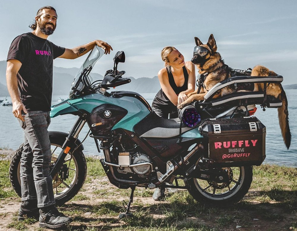 Greg and Jess Stone stand alongside late dog, Moxie. All three pose before a BMW adventure bike.