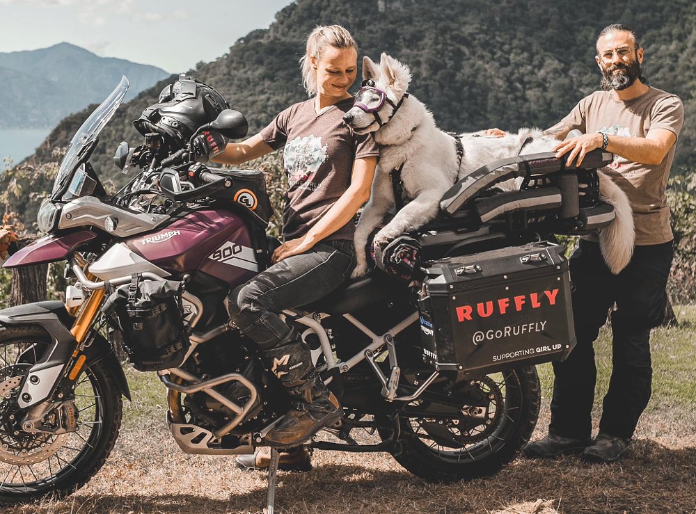Jess, Greg, and Whimsy stand before their Triumph adventure bike.