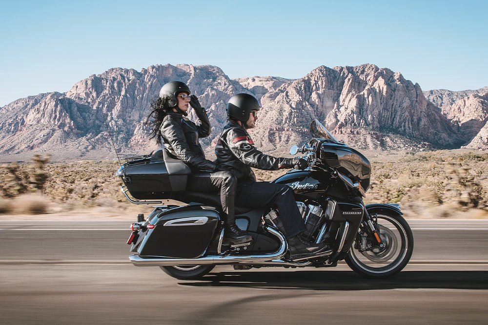 A couple rides two-up on the 2025 Indian Roadmaster PowerPlus with a mountain range in the background.
