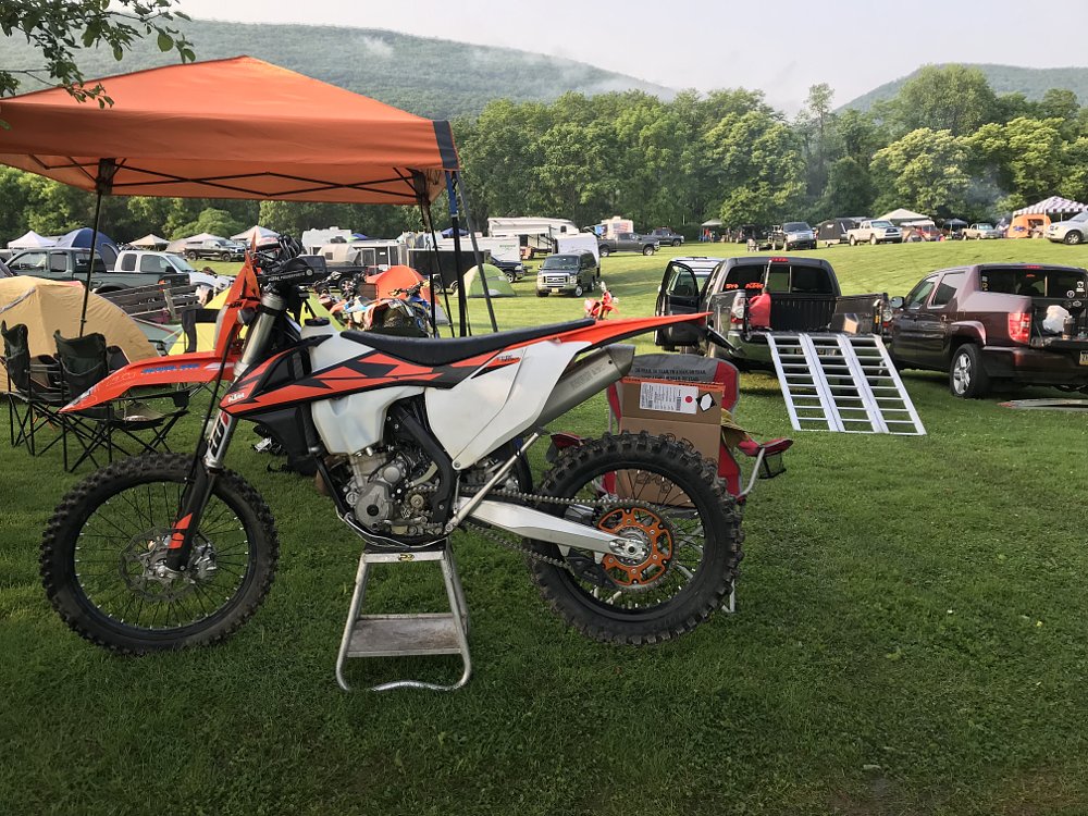 A KTM 350 EXC sits in a field at an amateur dirt bike race, surrounded by temporary canopies and pickup trucks.