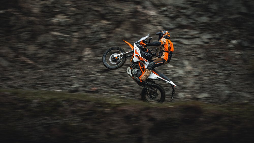 A 390 Adventure R rider performing a wheelie on a dirt trail.