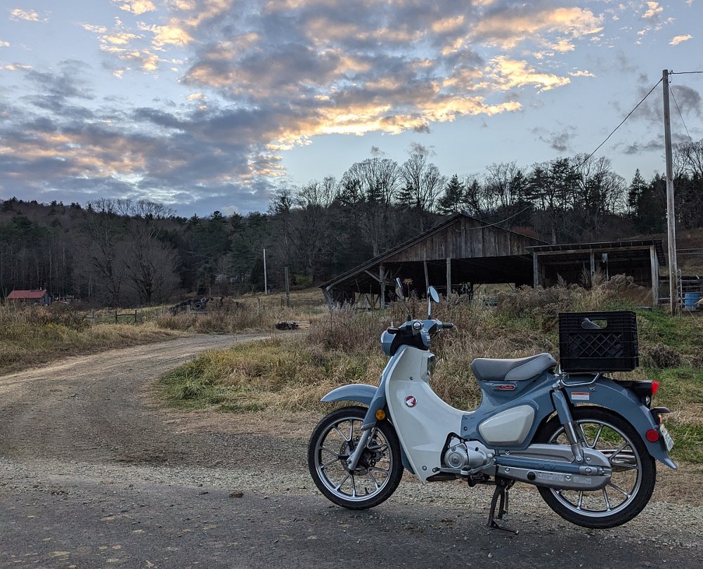 Super Cub along a rural road, an old barn in the background