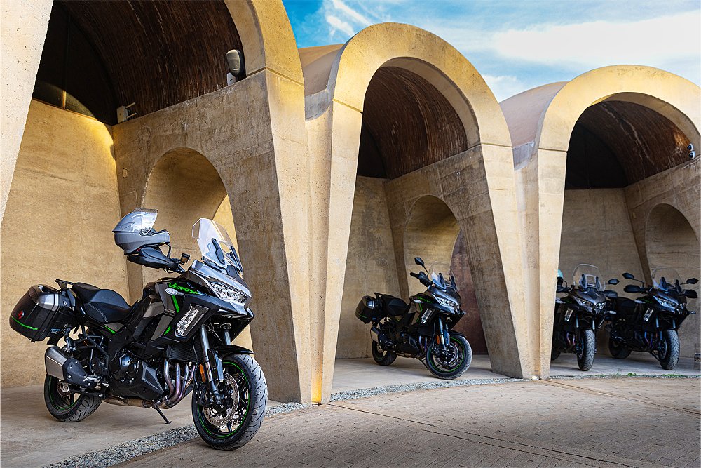 Several Versys 1100 SE LTs parked under the arches of a concrete building.