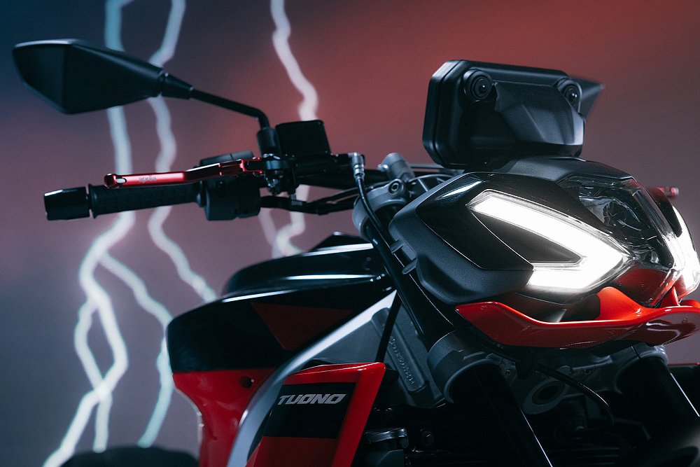 A close-up of the Tuono 457's headlight with lighting in the background.