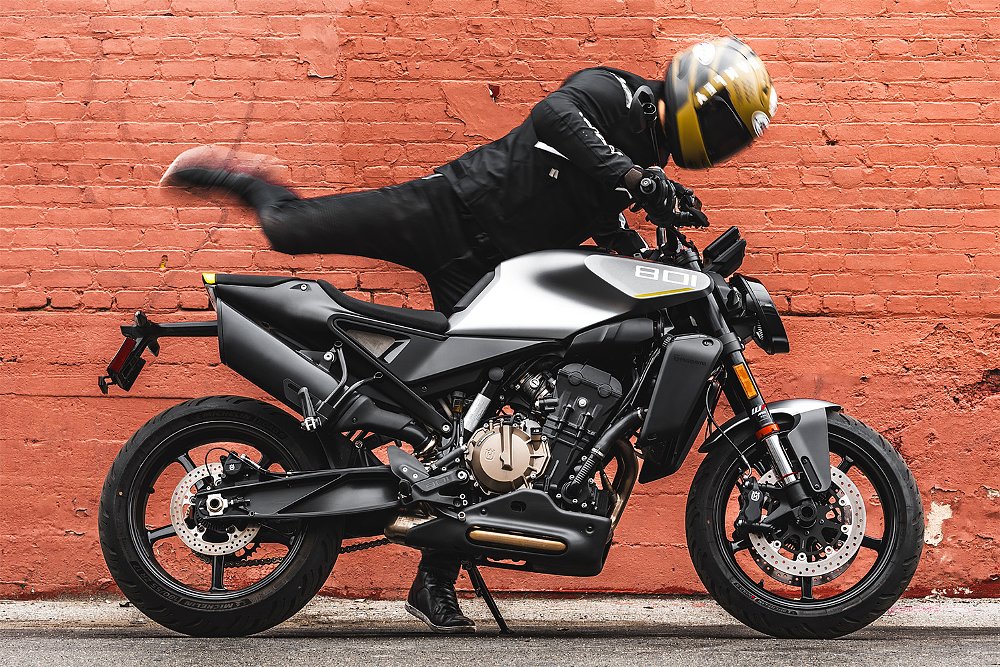 Dustin throws his leg over the Vitpilen 801 before a red brick wall.