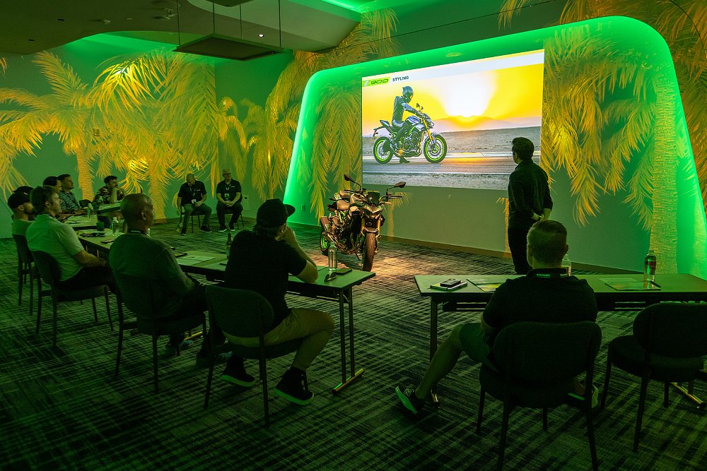 Moto journalists absorb the Kawasaki Z900 press launch presentation in a dimly lit hotel conference room.