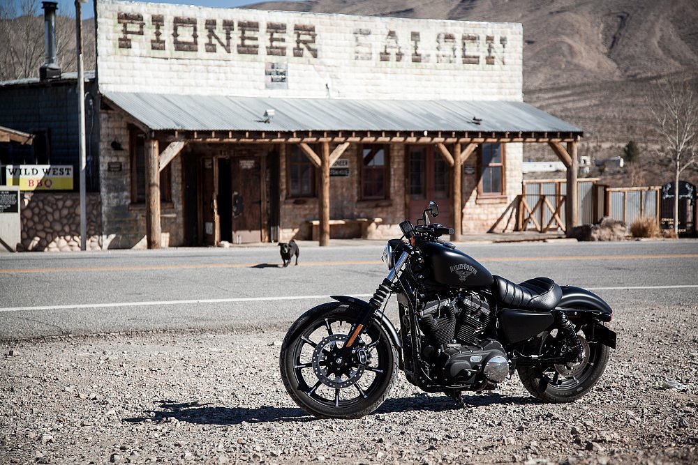 basic black Sportster parked in front of a weathered wooden building