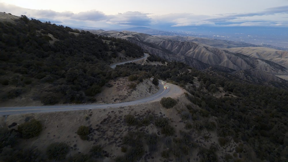 A mountain road winds down a hillside, with two motorcycles riding on it.