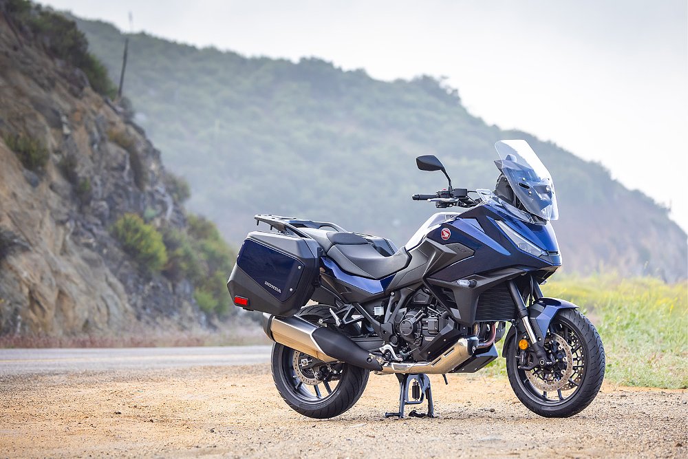 The 2025 Honda NT1100 DCT on its centerstand along a mountain road.