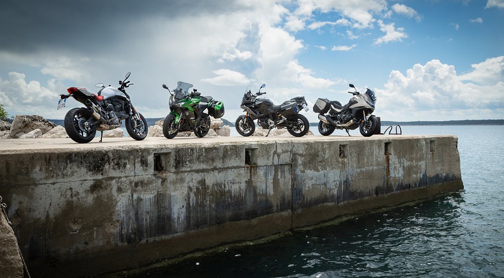 row of various motorcycles parked by a lake
