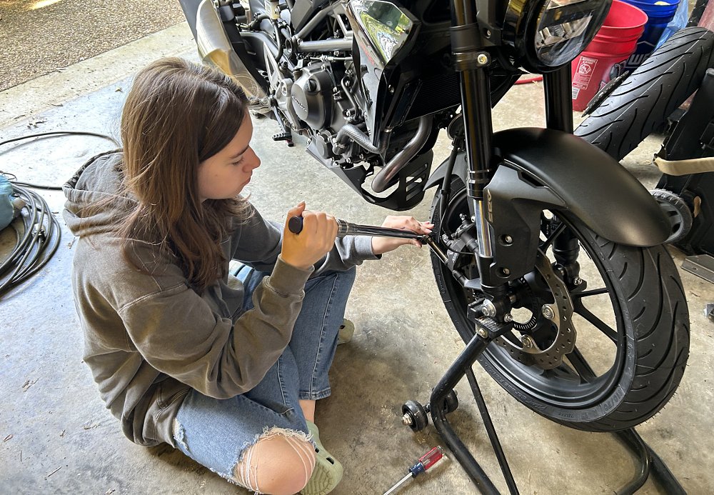 the teenage girl working on her motorcycle's brakes