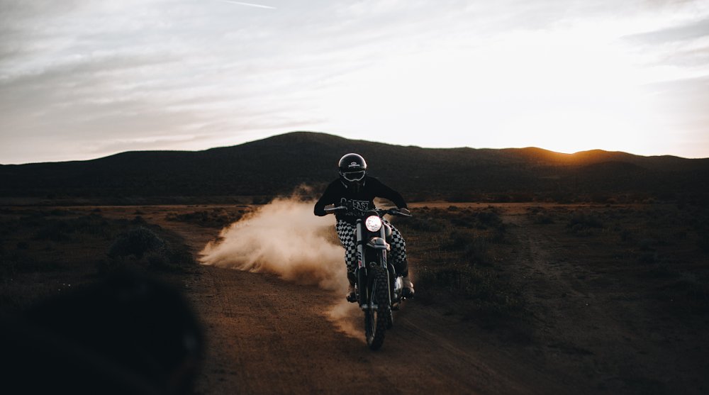 rider on a dirt trail at sunset, dust flying off his rear tire