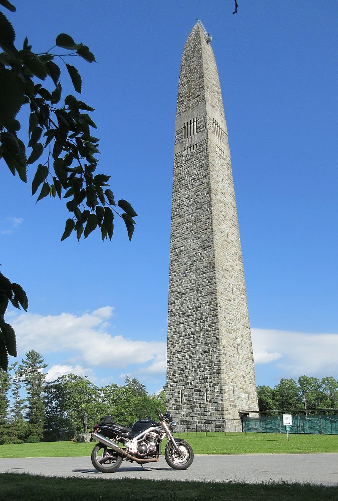 black motorcycle parked in front of the 306-foot-tall stone monument on a sunny summer day