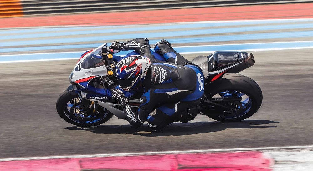 rider on a blue and white GSX-R1000 on the track leaned over in a curve