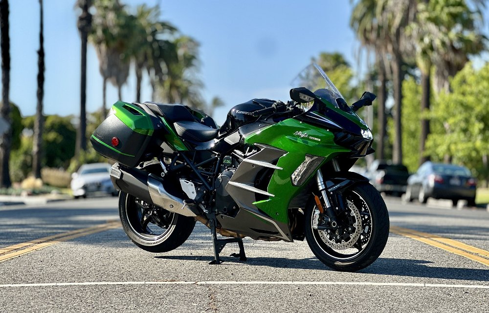 2025 Kawasaki H2 SX SE parked on its centerstand on a street lined with palm trees.