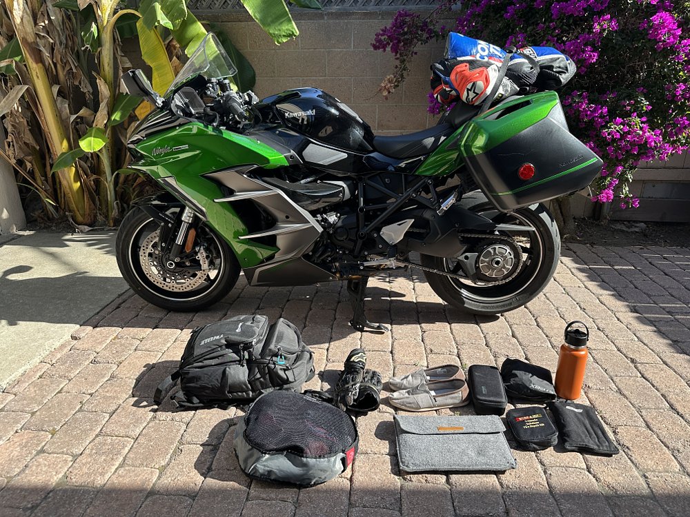 Kawasaki H2 SX SE parked in a driveway with items that fit in the saddlebags displayed in the foreground.