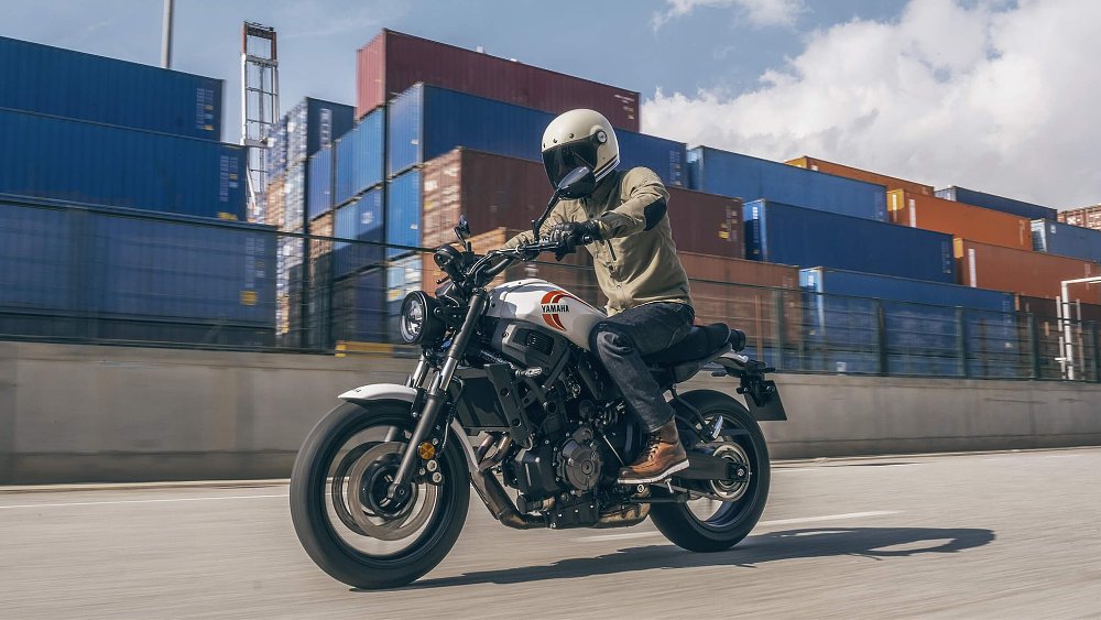 A motorcycle rider guides the Yamaha XSR700 past shipping containers in a container yard.