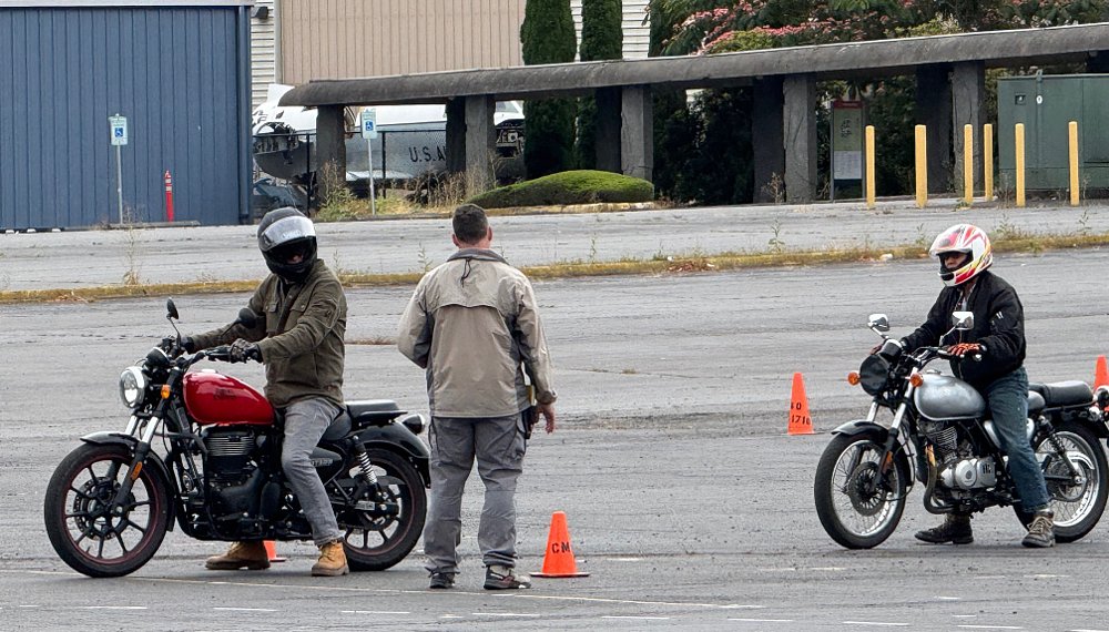 instructor in a parking lot watching two students on small motorcycles
