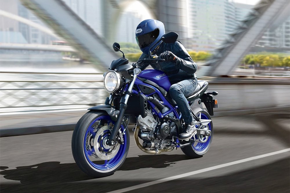 An SV650 rider zooms over a bridge in an urban area.