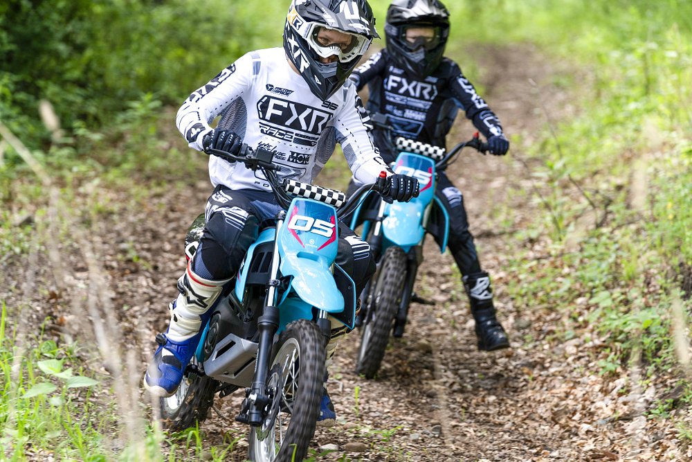 two kids riding blue CFMOTO dirt bikes on a trail
