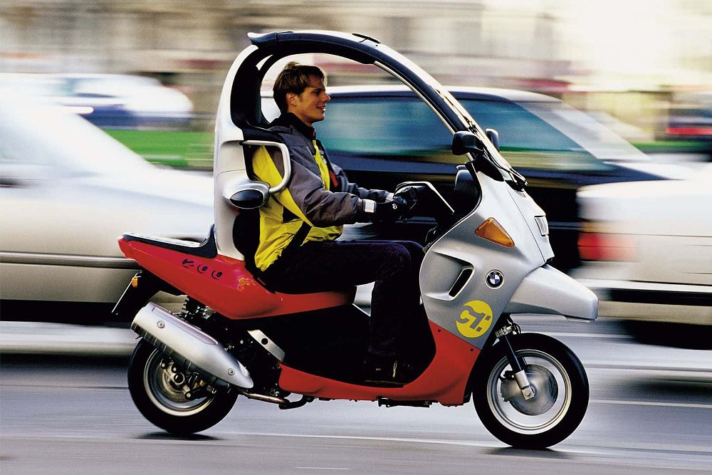 A casually dressed rider guides the BMW C1 enclosed scooter through an urban landscape.