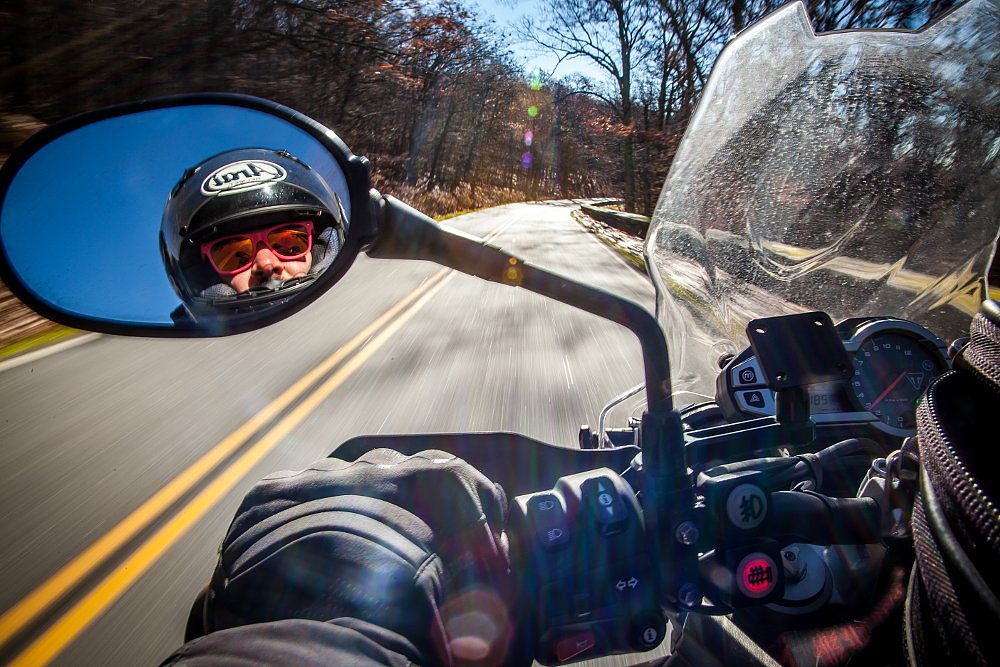 view of Spurgeon's rearview mirror as he's riding, showing his helmet and goofy colorful sunglasses in the mirror