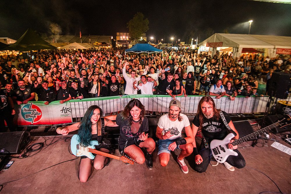 A band poses for the camera with cheering fans in the background.