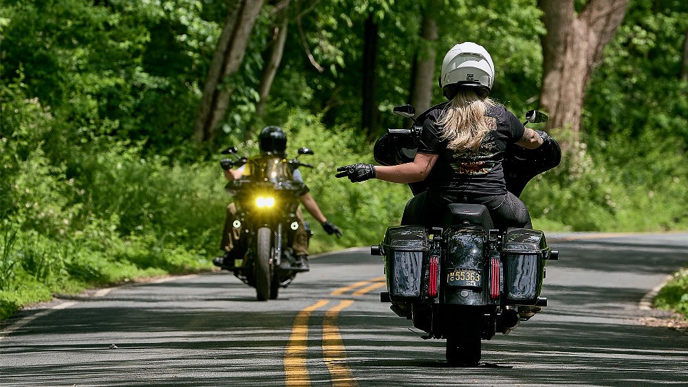 Two Harley riders exchange peace signs on a rural road.