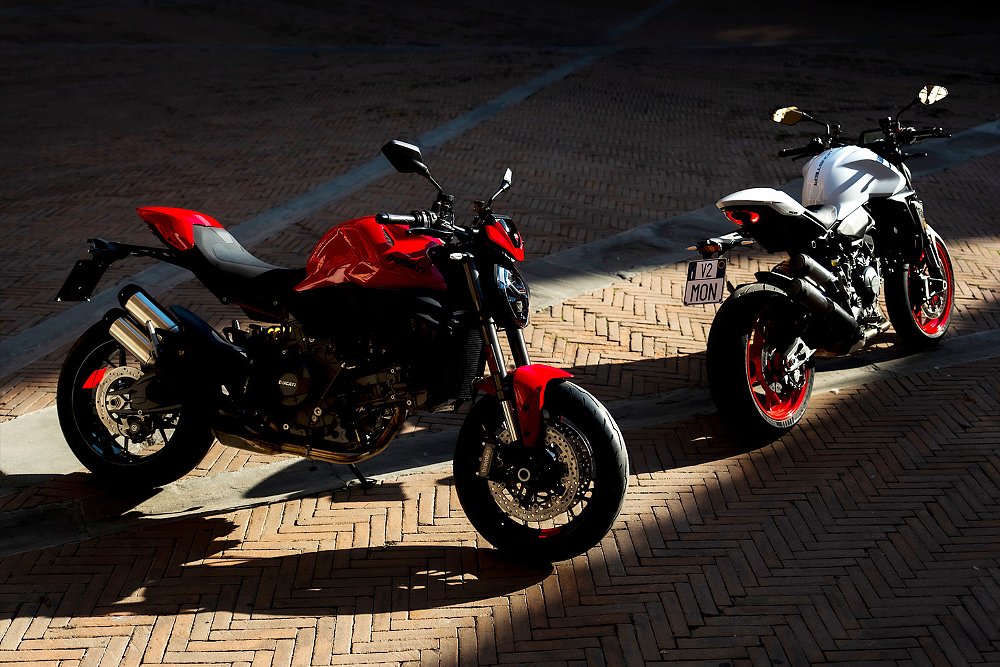 Two Ducati Monster+ motorcycles staged in a courtyard.